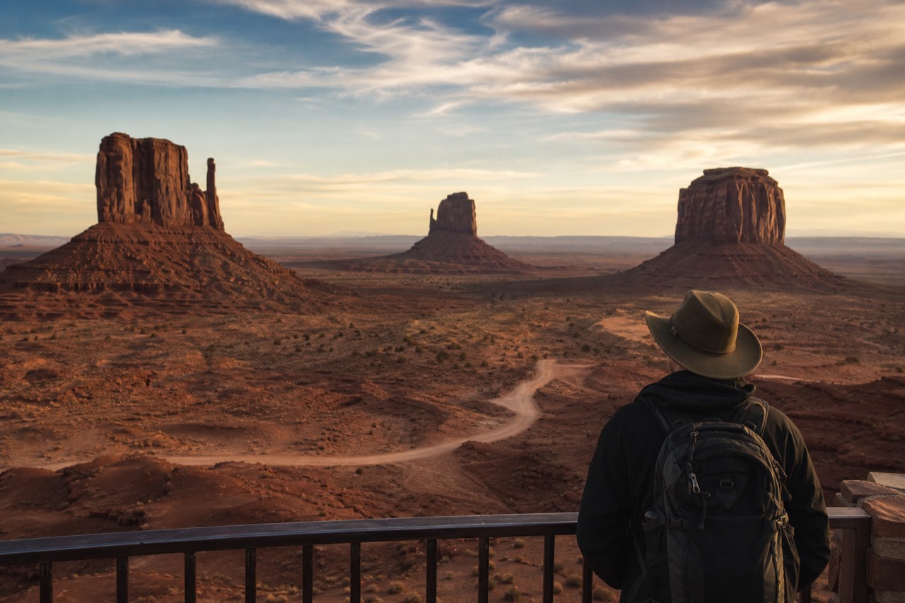 A lone traveler at a Monument Valley overlook looking out over the buttes at golden hour