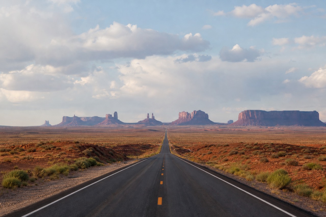 The straight highway US-163 running toward the red buttes of Monument Valley, the cinematic road view