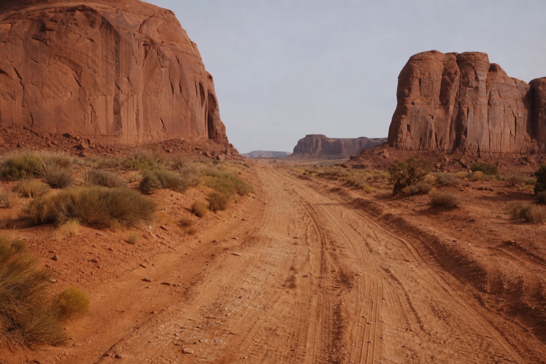 The rough washboard dirt of the 17-mile Valley Drive cutting through deep sand between buttes under flat midday light