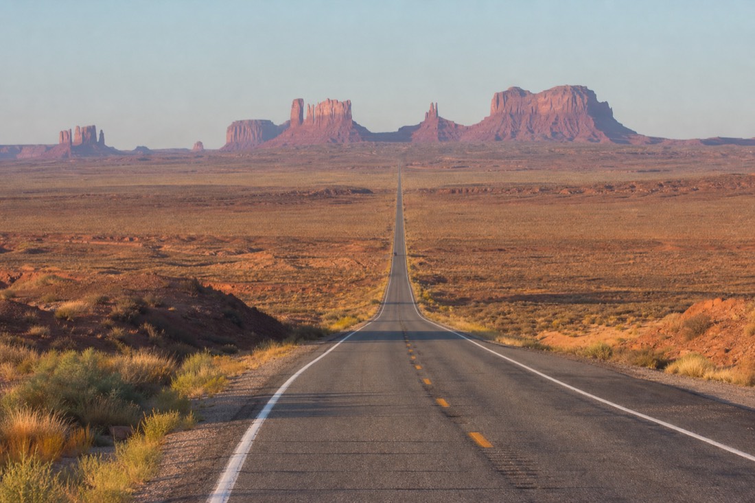 The straight US-163 highway running dead toward the distant buttes of Monument Valley across empty desert