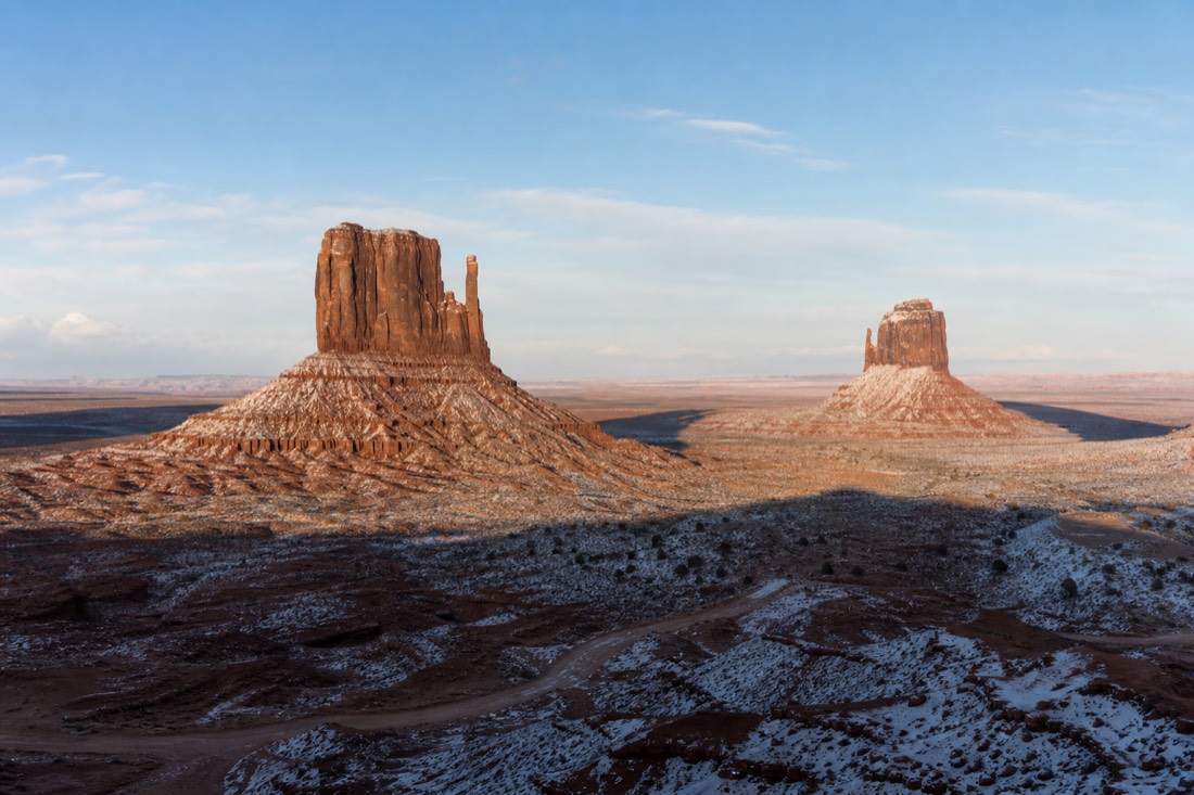 The twin Mitten Buttes lightly dusted with snow under a pale blue winter sky with long morning shadows