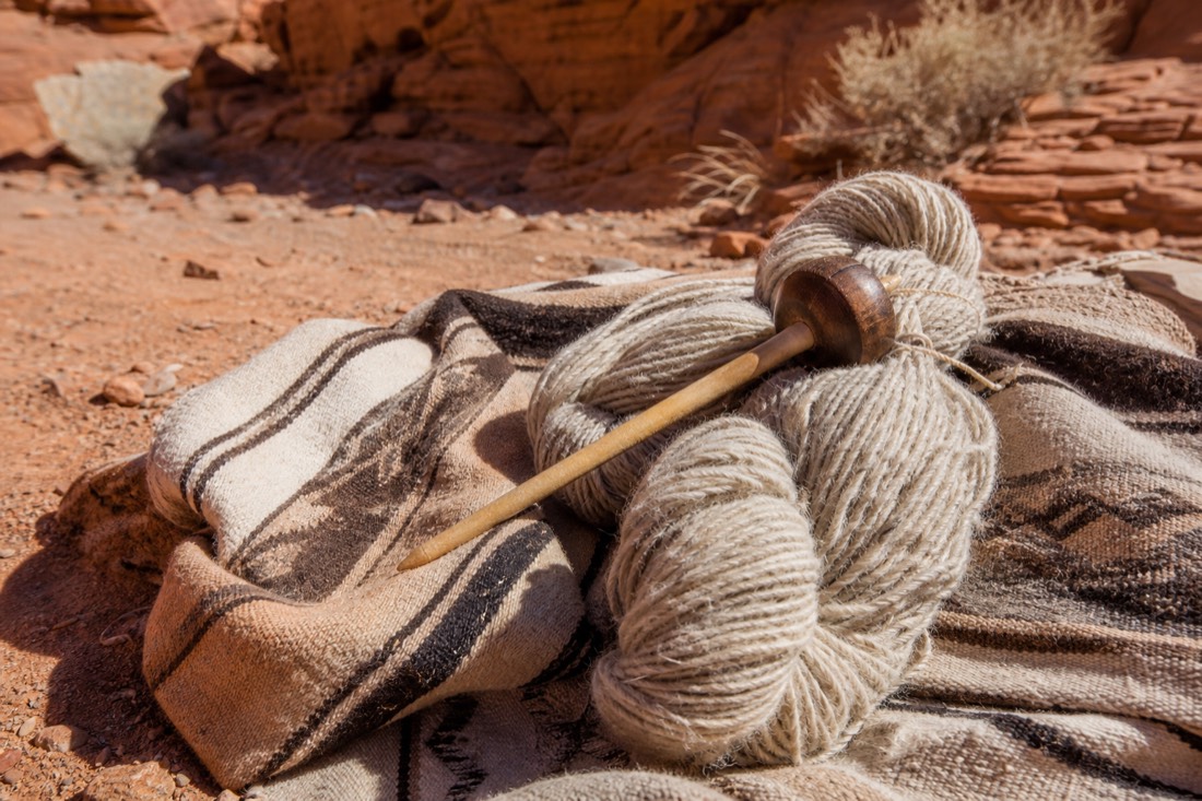 A spindle and skeins of handspun natural wool resting on a woven blanket in warm desert light