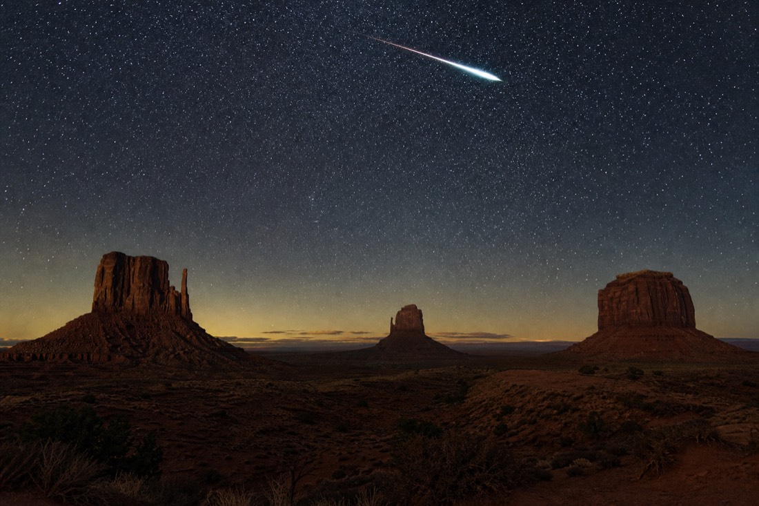 A brilliant meteor streaking across a star-filled desert sky above the dark outlines of Monument Valley buttes