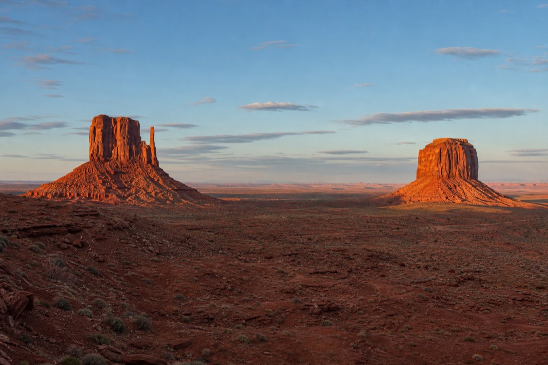 First light of sunrise striking the East and West Mitten Buttes head-on across the empty desert floor