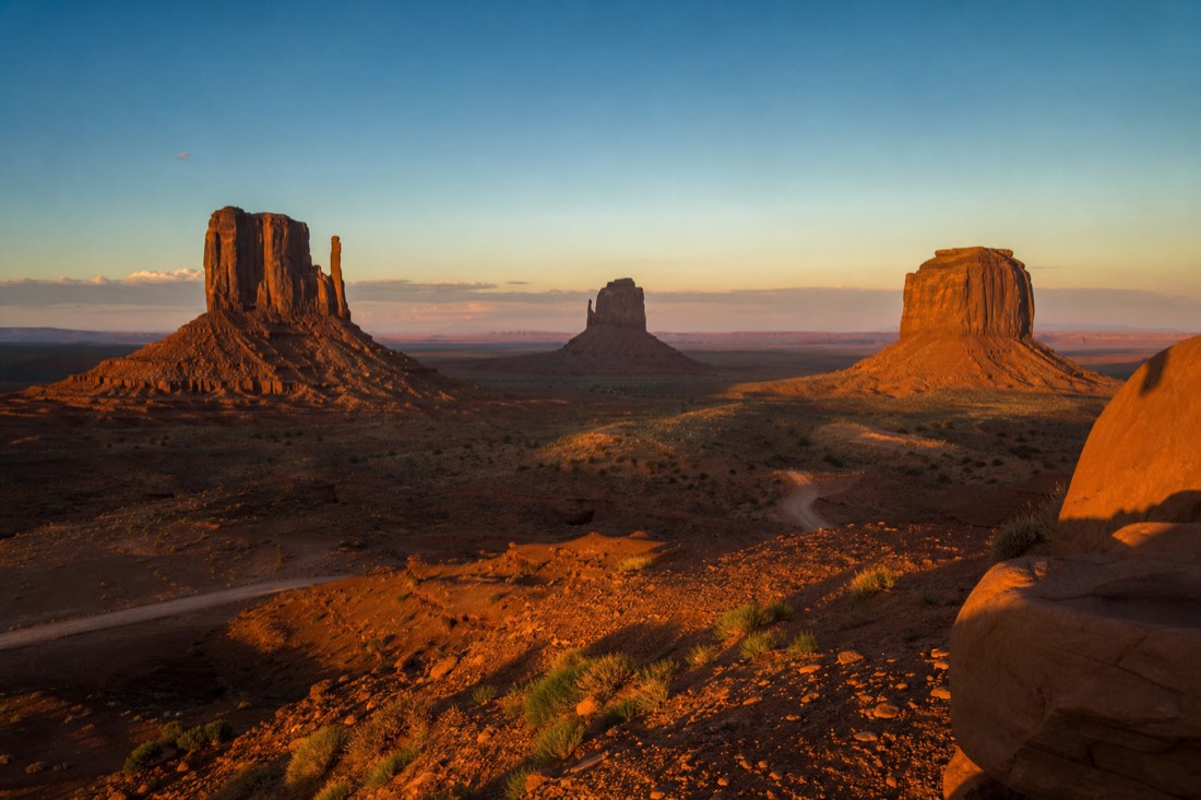 Long golden evening light stretching shadows across the Monument Valley floor beneath the buttes in late summer
