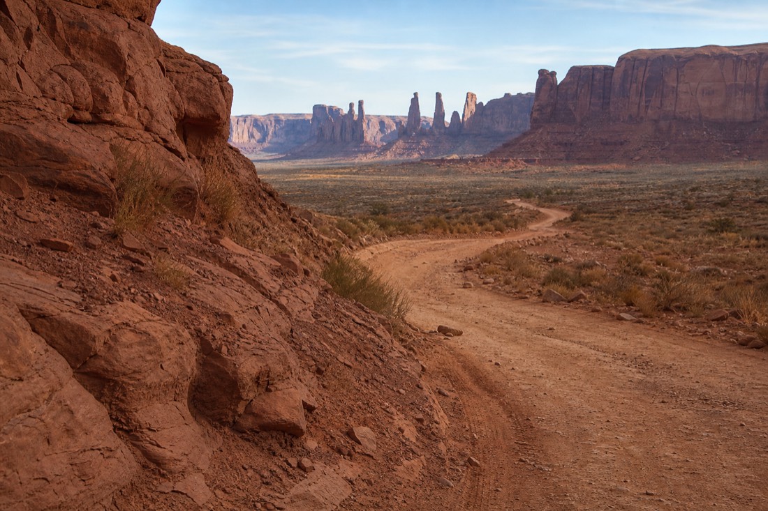 A rough sandy backcountry track curving toward a group of thin rock pinnacles deep in Monument Valley