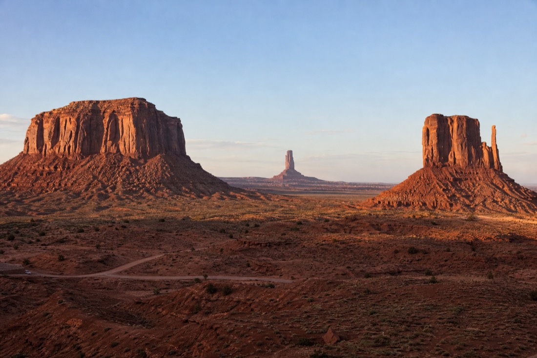 Wide Monument Valley panorama contrasting broad flat-topped mesas and the two Mitten Buttes with a slender distant spire