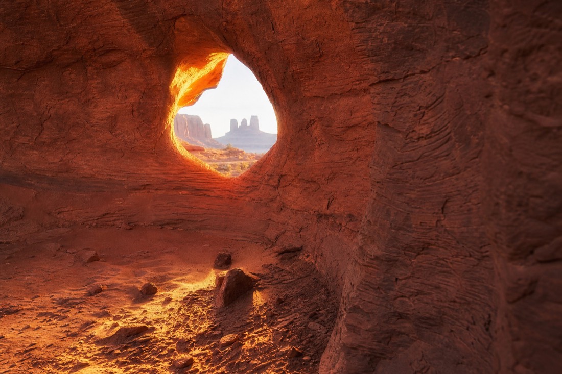 Sun's Eye, a natural rock opening in a sandstone wall glowing with warm light in Monument Valley's backcountry