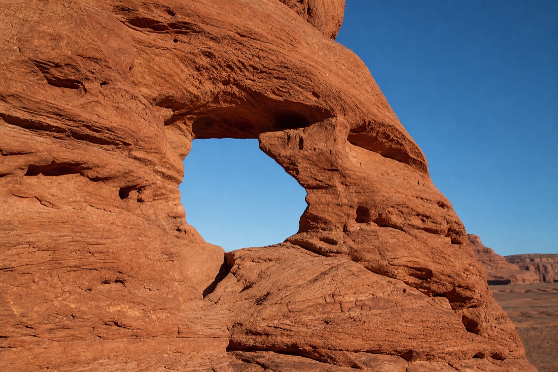 The Ear of the Wind arch framing a patch of blue sky in a sandstone wall of Monument Valley's backcountry