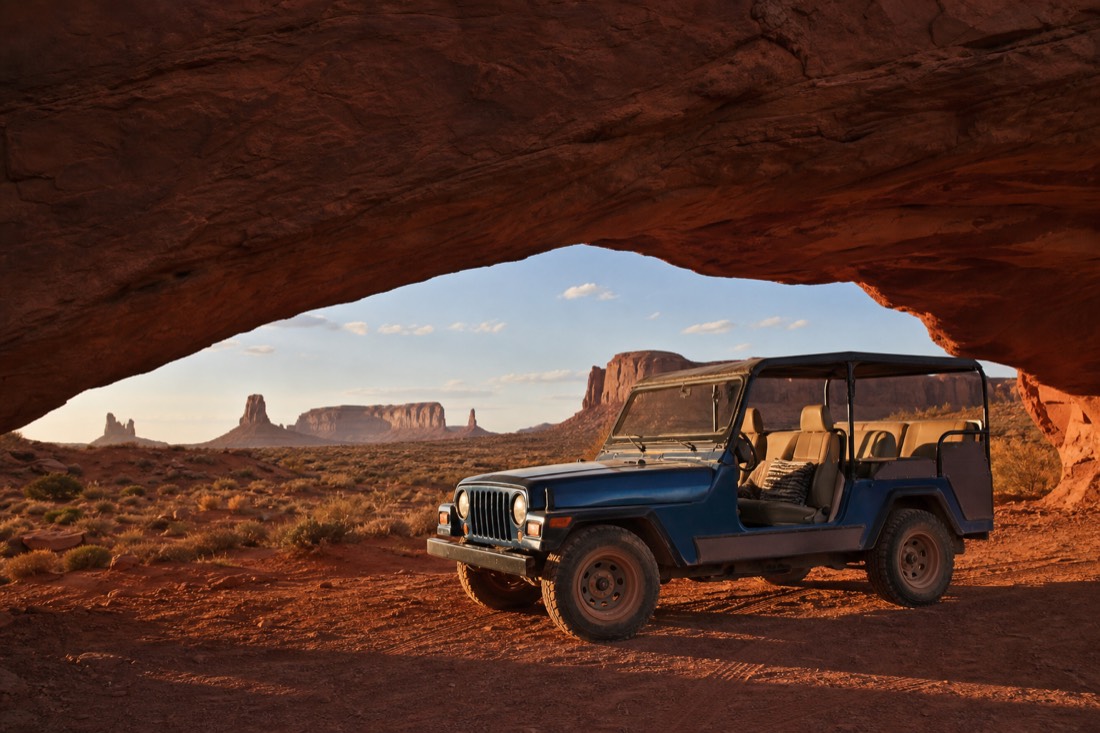 An open-air Navajo jeep parked beneath a red sandstone arch in the Monument Valley backcountry