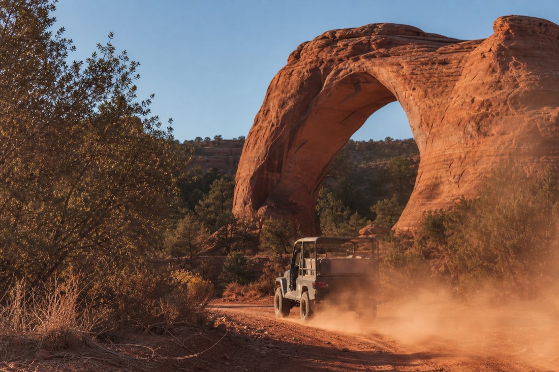 An open-air Navajo jeep raising a plume of red dust on a backcountry trail past the loop