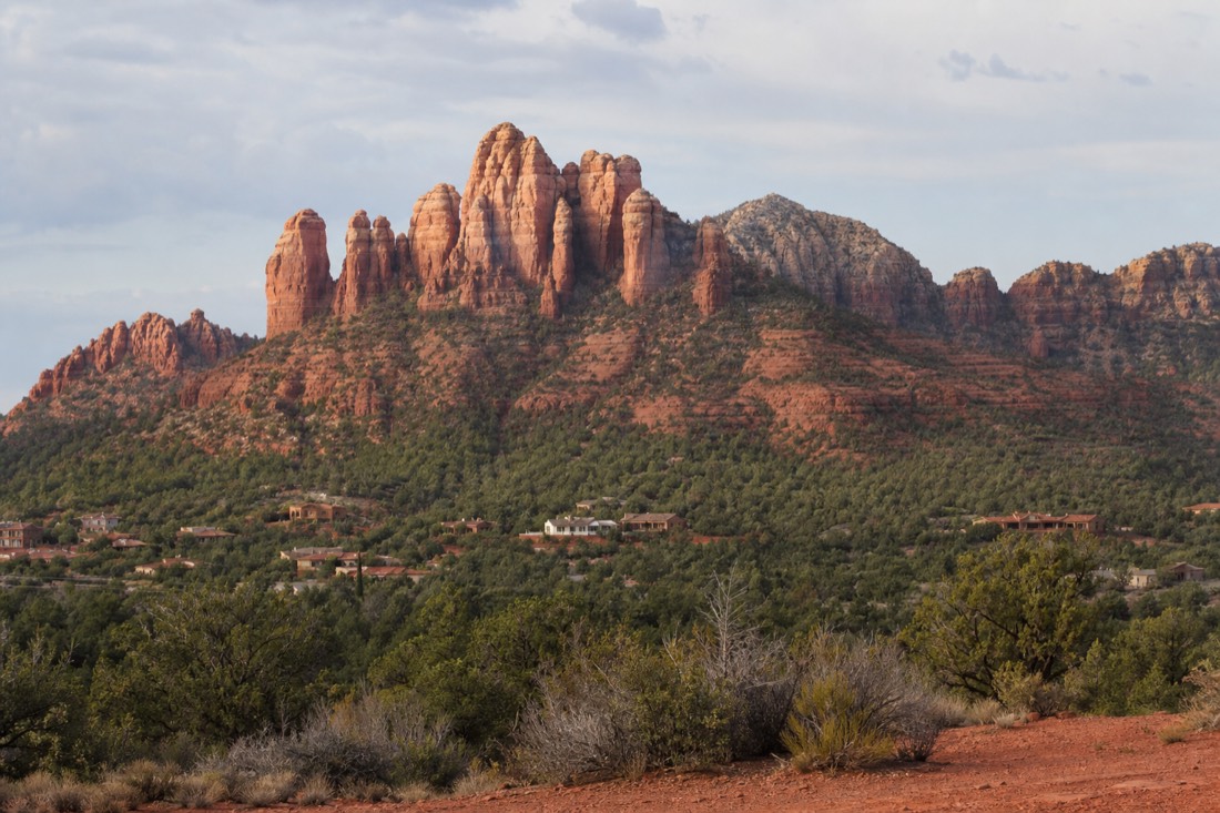 Towering red sandstone rock formations rising above green pinyon and juniper scrub near a small desert town