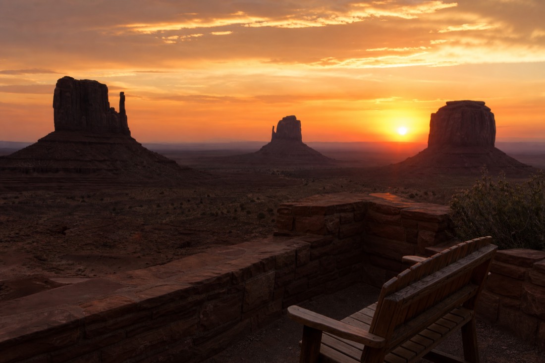 A lodge terrace overlooking the Mitten buttes at sunset, the sky glowing orange over the darkening valley