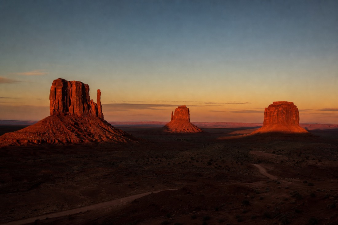 The three tall Mitten buttes catching deep red sunset light while the valley floor falls into shadow