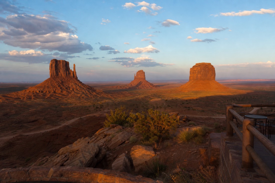 Warm evening light turning the Mitten buttes deep red as long shadows stretch across the valley floor beneath a lodge terrace