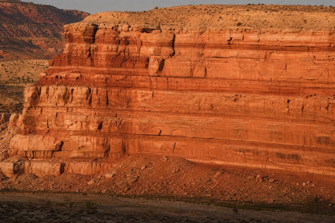 Cross-section view of layered red and orange sandstone cliffs revealing horizontal erosion bands in warm afternoon light