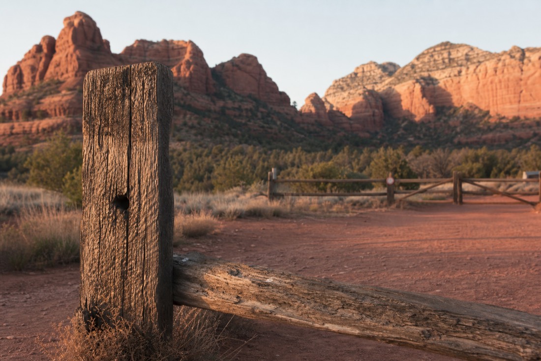 A weathered wooden park boundary marker at a quiet desert gate with red buttes rising beyond