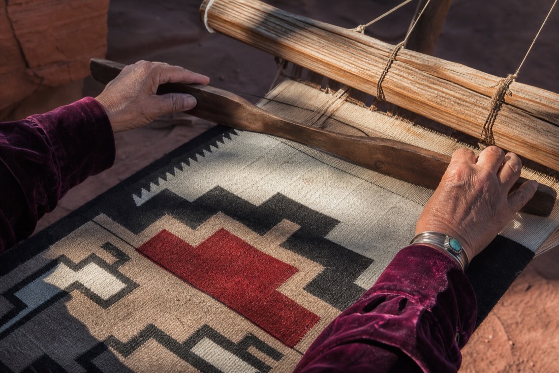 Hands weaving a traditional Navajo textile on a wooden loom with desert light falling across the wool