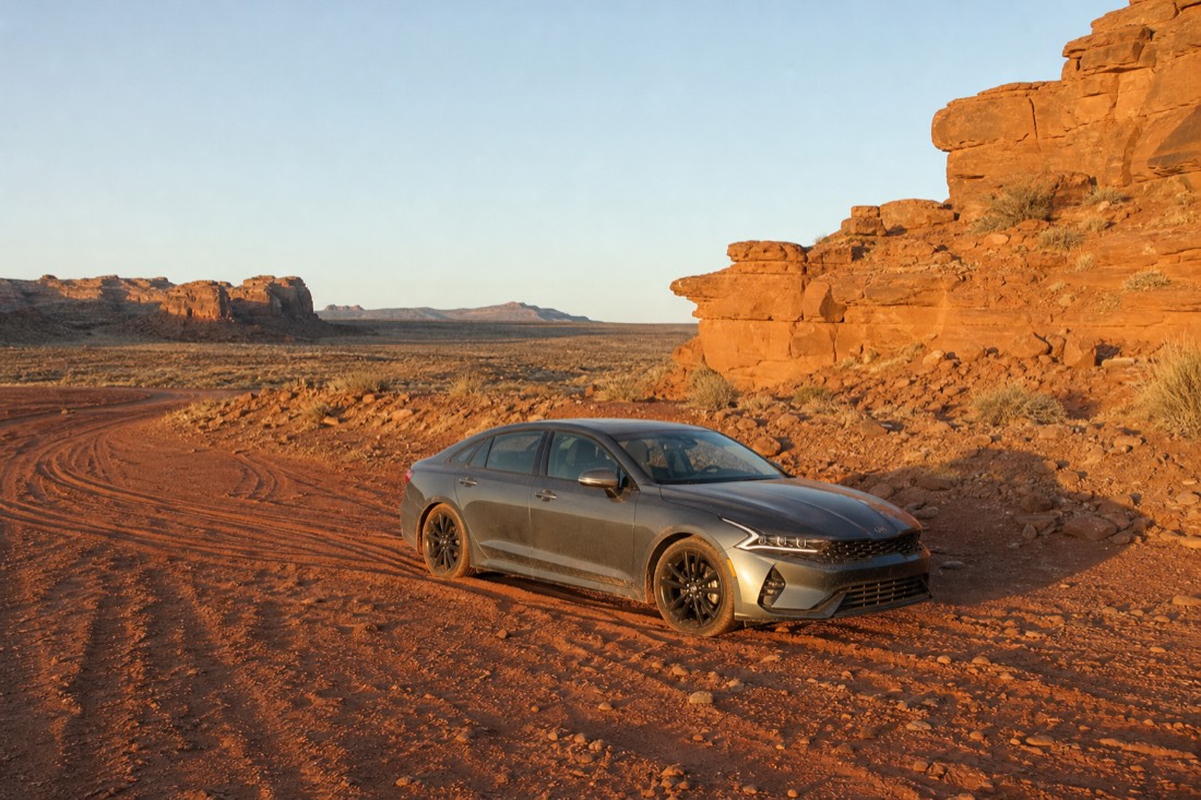 A low sedan stopped in a patch of deep red sand on the loop road with tire tracks curving behind it