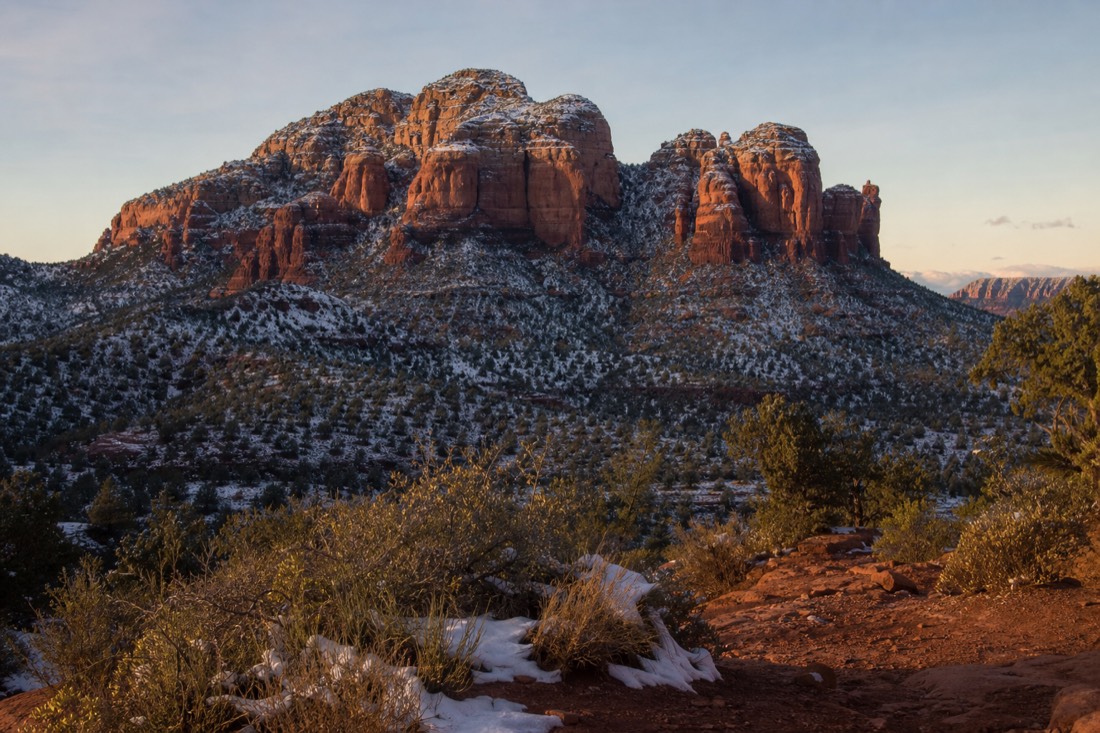 A light dusting of snow on the red buttes under a pale winter sky with long low shadows