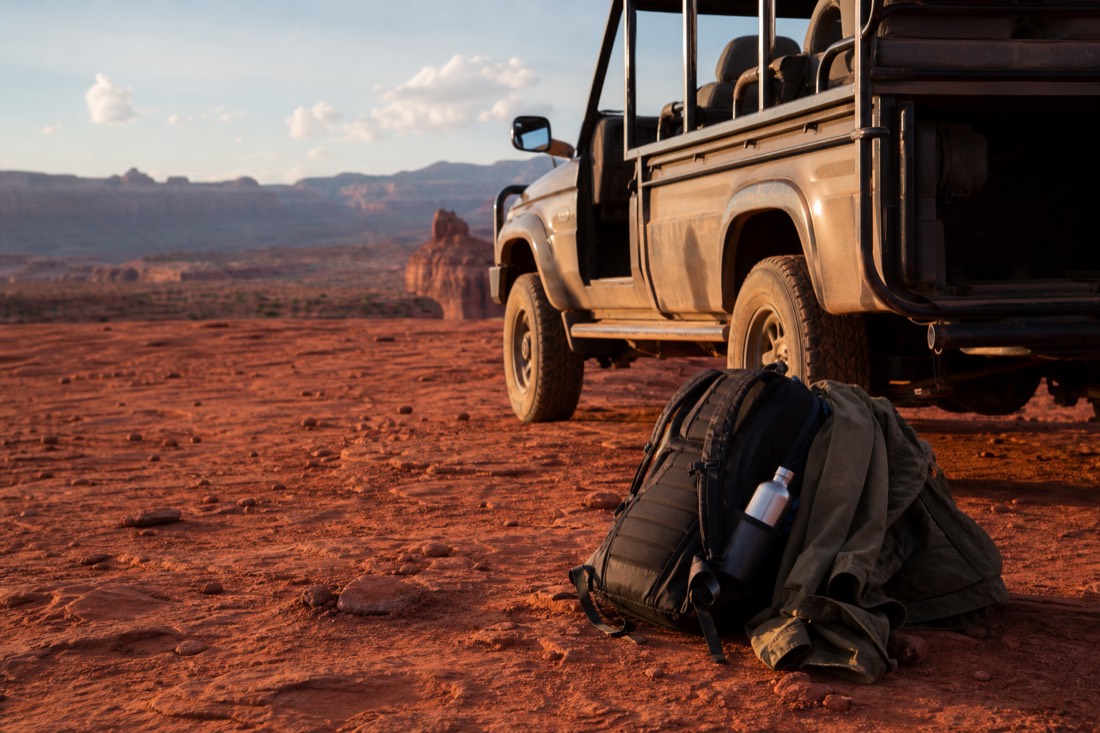 A daypack with a water bottle and a jacket resting on red sand beside an open-air tour vehicle