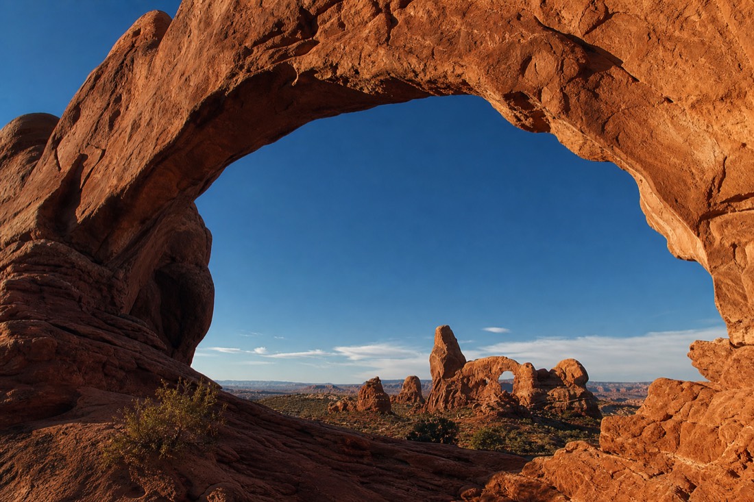 A tall stone arch framing distant desert spires under a deep blue sky in the Utah canyon country