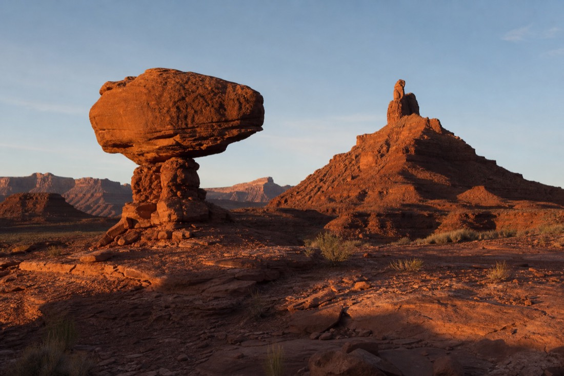 A balanced rock and a hen-shaped butte catching low golden light, deep shadows across the desert floor