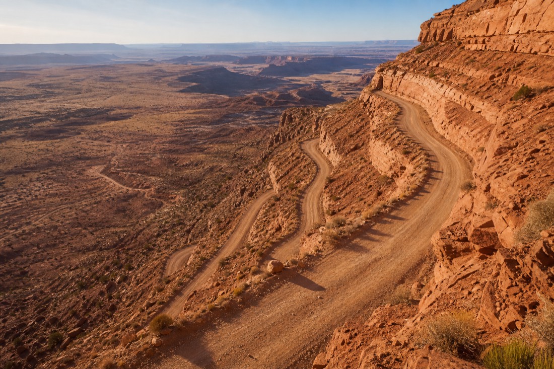 Gravel switchbacks of the Moki Dugway climbing a red cliff face above a wide desert basin, canyon country stretching to the horizon