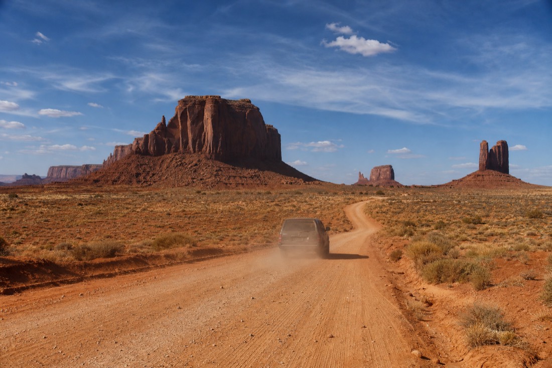 A vehicle on the washboard dirt scenic loop road inside Monument Valley Navajo Tribal Park